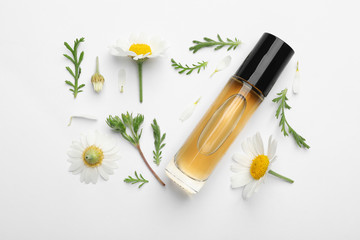 Composition with chamomile flowers and cosmetic bottle of essential oil on white background, top...