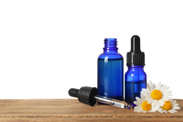 Chamomile flowers and cosmetic bottles of essential oil on wooden table against white background....