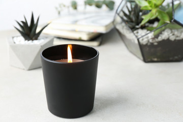 Burning candle and plants on white table, space for text