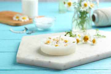 Board with floral candle and chamomile on color wooden table