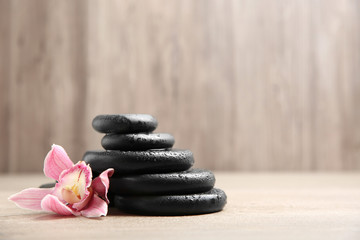 Fototapeta na wymiar Stack of black spa stones with flower on wooden background. Space for text