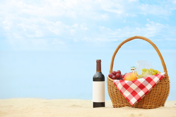 Wicker basket with food and wine on sand near sea, space for text. Beach picnic