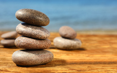 Fototapeta na wymiar Stack of stones on wooden table against seascape, space for text. Zen concept