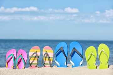 Obraz premium Composition with bright flip flops on sand near sea in summer. Beach accessories