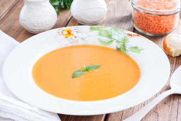 Red lentil cream soup in a white plate on a wooden table, horizontal