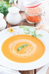 Red lentil cream soup in a white plate on a wooden table, selective focus