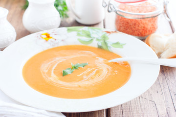 Red lentil cream soup in a white plate on a wooden table, horizontal