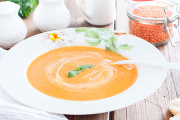 Red lentil cream soup in a white plate on a wooden table, horizontal