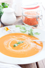 Red lentil cream soup in a white plate on a wooden table, selective focus