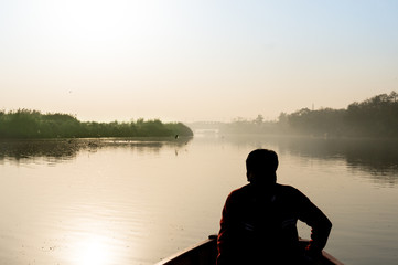 silhouette of boatsman rowing out into the yamuna ganga river in the morning