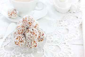 Useful candies of dried fruits in coconut chips in the form of balls on a white table, horizontal, copy space