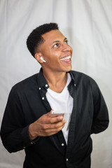 Happy African American young handsome man with wireless earphones in black shirt holding smartphone and laughing