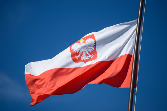 The state flag of Poland with the emblem of the Republic of Poland, on a background of blue sky, in the wind.