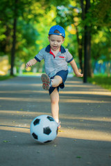 The boy plays football in the city Park on the sidewalk . The child gives the ball a pass makes a feint and enthusiastically leads the soccer ball