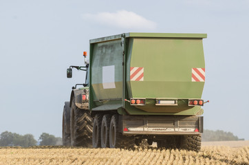 AGRICULTURAL MACHINE -  Modern large farm tractor with a trailer for grain transport works in the field during harvest time