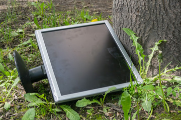 A broken and outdated monitor thrown into the street under a tree