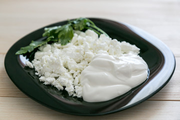 Cottage cheese with sour cream on a black plate. Black glass plate with cottage cheese and sour cream a wooden background.,