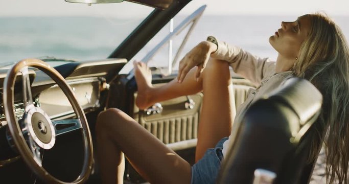 Attractive woman sitting in the passenger seat of a classic vintage car looking into the camera, model posing naturally in a vintage car, woman enjoying a coastal road trip