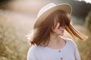 Stylish girl in rustic dress smiling and waving hair in sunny meadow in mountains. Portrait of...