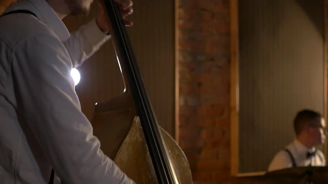 The guy plays a double bass at the studio. Macro shooting of strings and stamp. The music band plays in the restaurant. Night is a romantic light. Jazz, Blues, Funk Retro studio, brick interior.