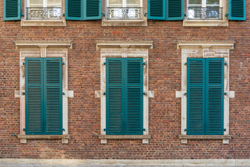 Beautiful vintage exterior of building with old rough brick wall facade and elegant windows which consist of wooden green shutters, deluxe white concrete sash and frieze, and small balcony.