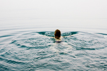 Fototapeta na wymiar Young beautiful woman is swimming in calm water. The calm water of the lake.