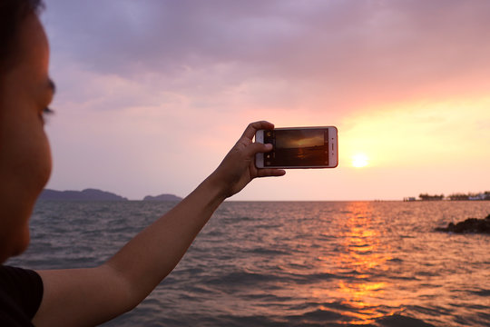 Woman taking a photo of the sunset with smartphone