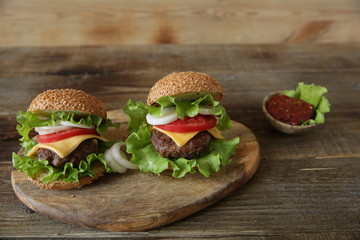 Two hamburger with beef cutlet, with cheese, pickles, tomatoes, onions, lettuce and tomato sauce in a saucer on a wooden rustic background with copy space for text.