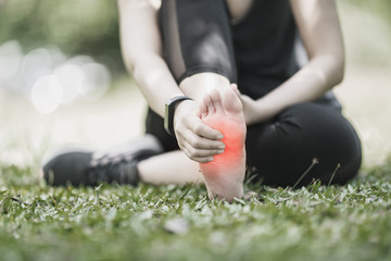 pain in foot, girl holds her hands to her feet, foot massage, cramp, muscular spasm, red accent on foot