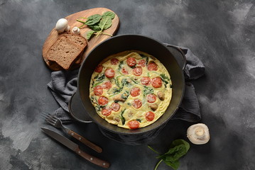 Frittata made of eggs, mushrooms, cherry tomatoes and spinach served in a pan. Italian cuisine.
