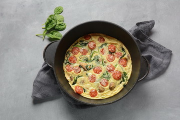 Fototapeta na wymiar Frittata made of eggs, mushrooms, cherry tomatoes and spinach served in a pan. Italian cuisine.