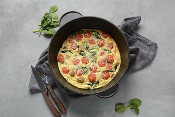 Obraz na płótnie Canvas Frittata made of eggs, mushrooms, cherry tomatoes and spinach served in a pan. Italian cuisine.