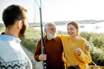 Young man and woman with senior grandfather dressed in sweaters spending a good time together while...