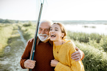 Portrait of a young woman with cheerful senior grandfather hugging together outdoors, having a good...