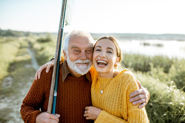 Portrait of a young woman with cheerful senior grandfather hugging together outdoors, having a good...