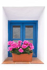 Fototapeta na wymiar Blue window with pink geranium flowers in a white village in the South of Spain