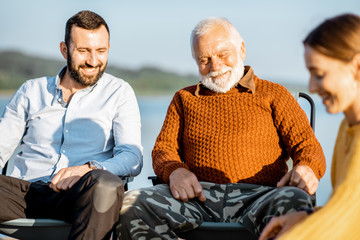 Man and woman having warm conversation with senior grandfather during the picnic near the lake in...