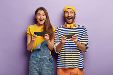 Joyful happy woman and man play games on smartphone, challenge each other, browse net, use...