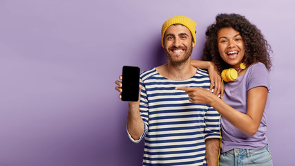 Selective focus of happy woman and man points to modern device with blank screen for your...