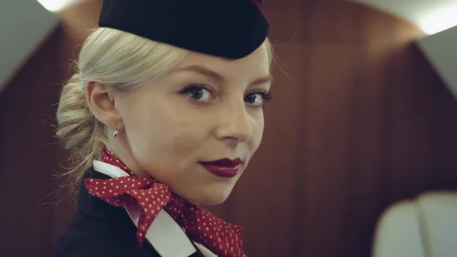 On a Plane Beautiful Blonde Stewardess/ Flight Attendant Smiles with Warm and Welcoming Smile. Airplane Looks New. Shot on RED EPIC Helium Cinema Camera.