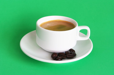 White coffee cup with coffee beans on green background