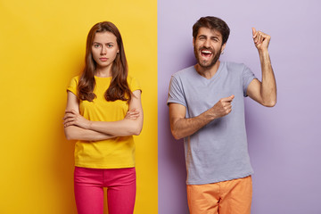 Happy cheering guy raises hands and dances happily, dissatisfied woman doenst pay attention to him, keeps hands crossed, angry after quarrel. Two colored background. People, facial expressions concept