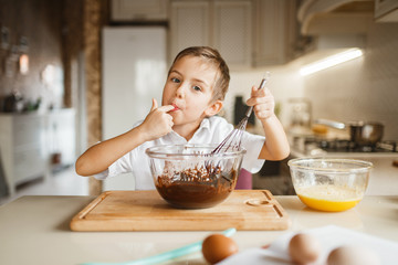 Male kid tastes melted chocolate in a bowl