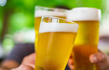 Close-up view of a three glass of beer in hand. Beer glasses clinking at outdoor bar or pub