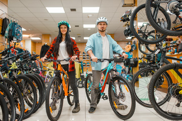 Couple in helmets choosing bicycles in sport shop