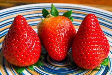 Three red strawberries fruit on colorful plate 