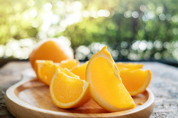 Sliced Orange on Wooden Plate. Fresh Juicy Fruit in Summer. Selective Focus. Blurred Tree with Lens Flare as background