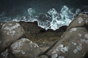 View from top point of rocky cliff: raging blue ocean with white foam centered in composition.