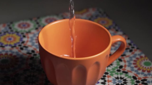  Italy - June 22, 2019: Slow motion hot water poured into an orange cup.