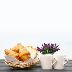 Croissant and cereal bread in wood basket for breakfast in the morning food or dessert and snack with two coffee or tea and cocoa in white cup and flower on black table and white background isolated